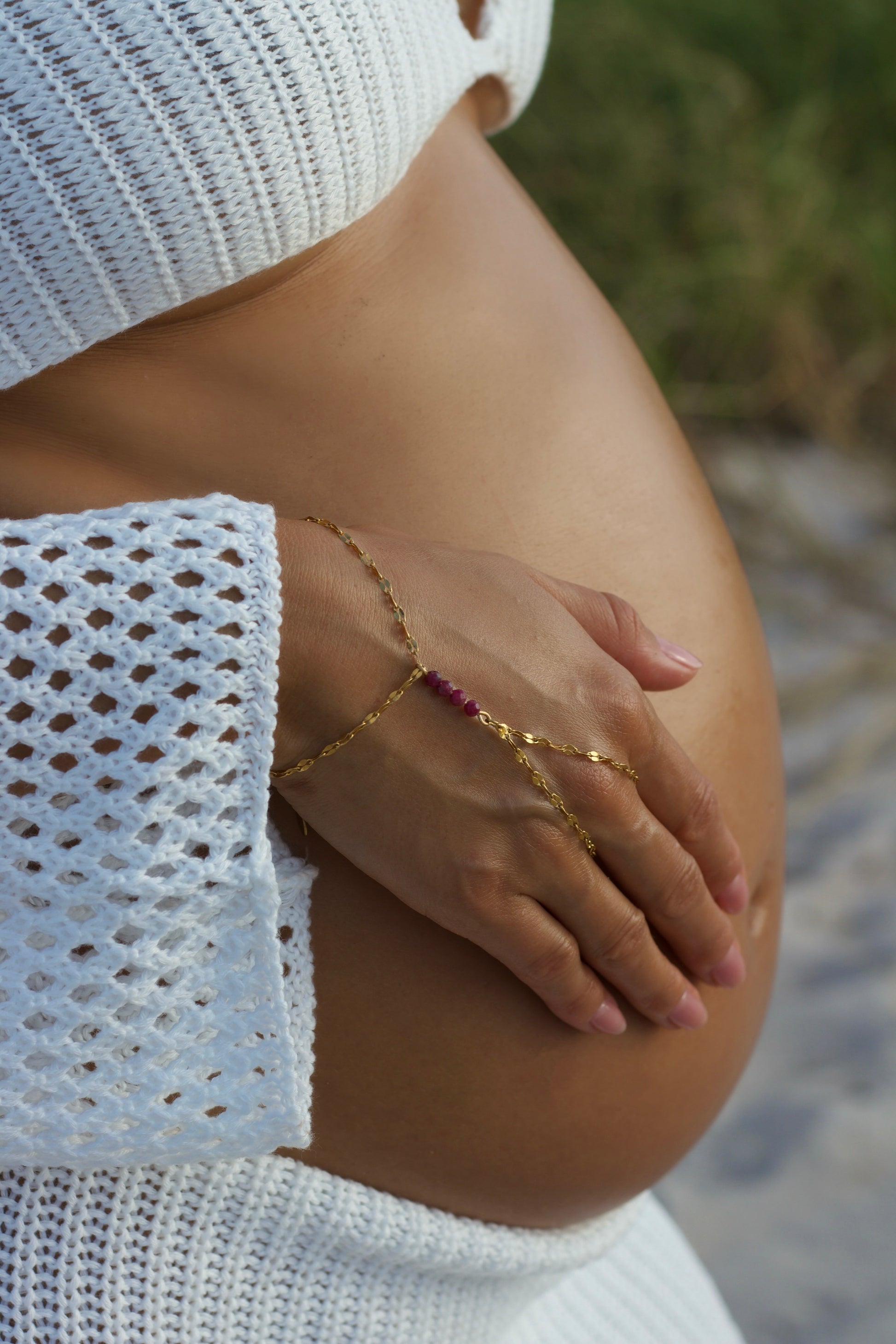 Pregnant belly with genuine ruby hand chain bracelet with blurred natural background