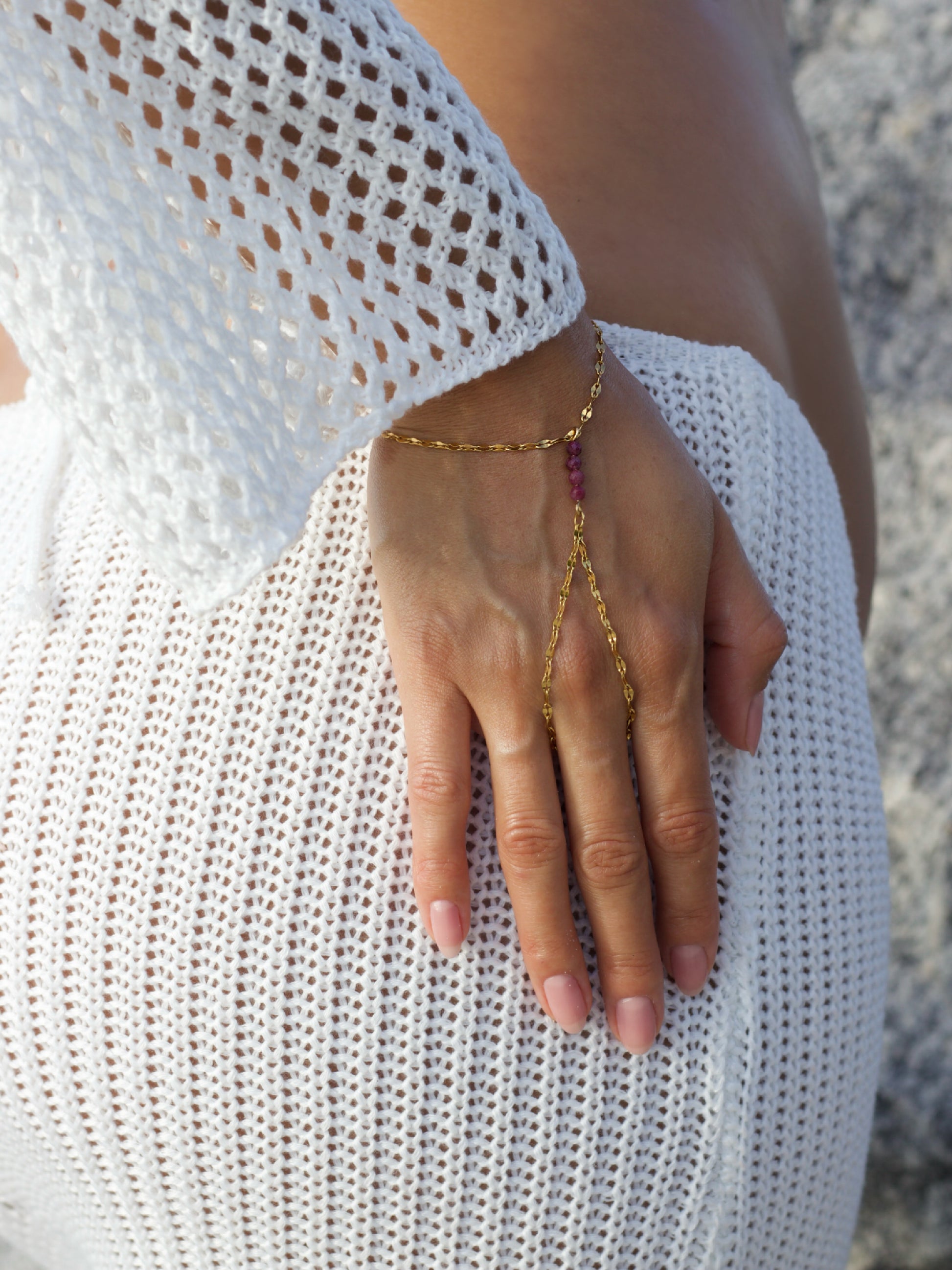 Hand wearing a gold hand chain bracelet with a blurred background