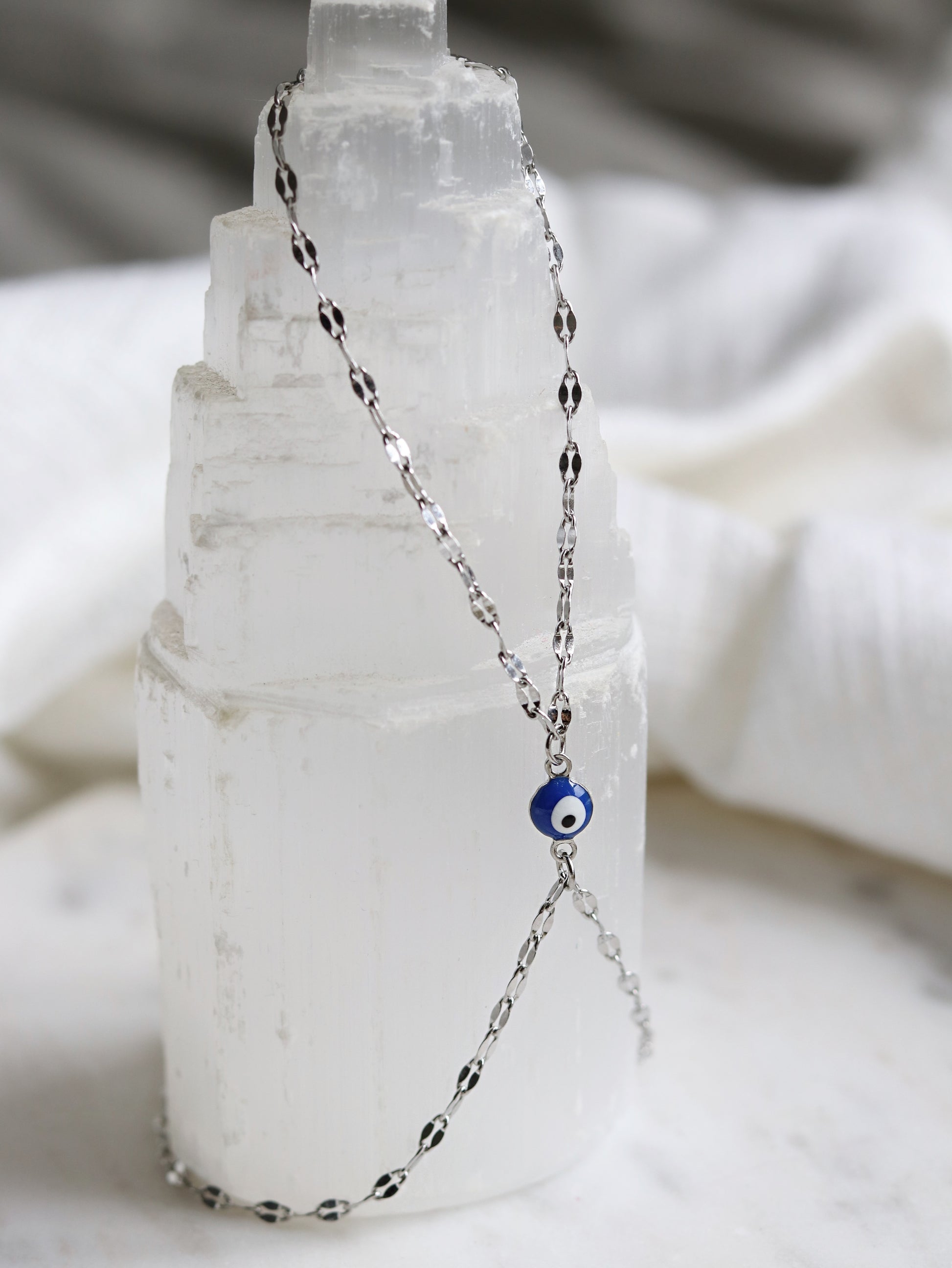 silver hand chain bracelet with a blue evil eye pendant on a selenite crystal