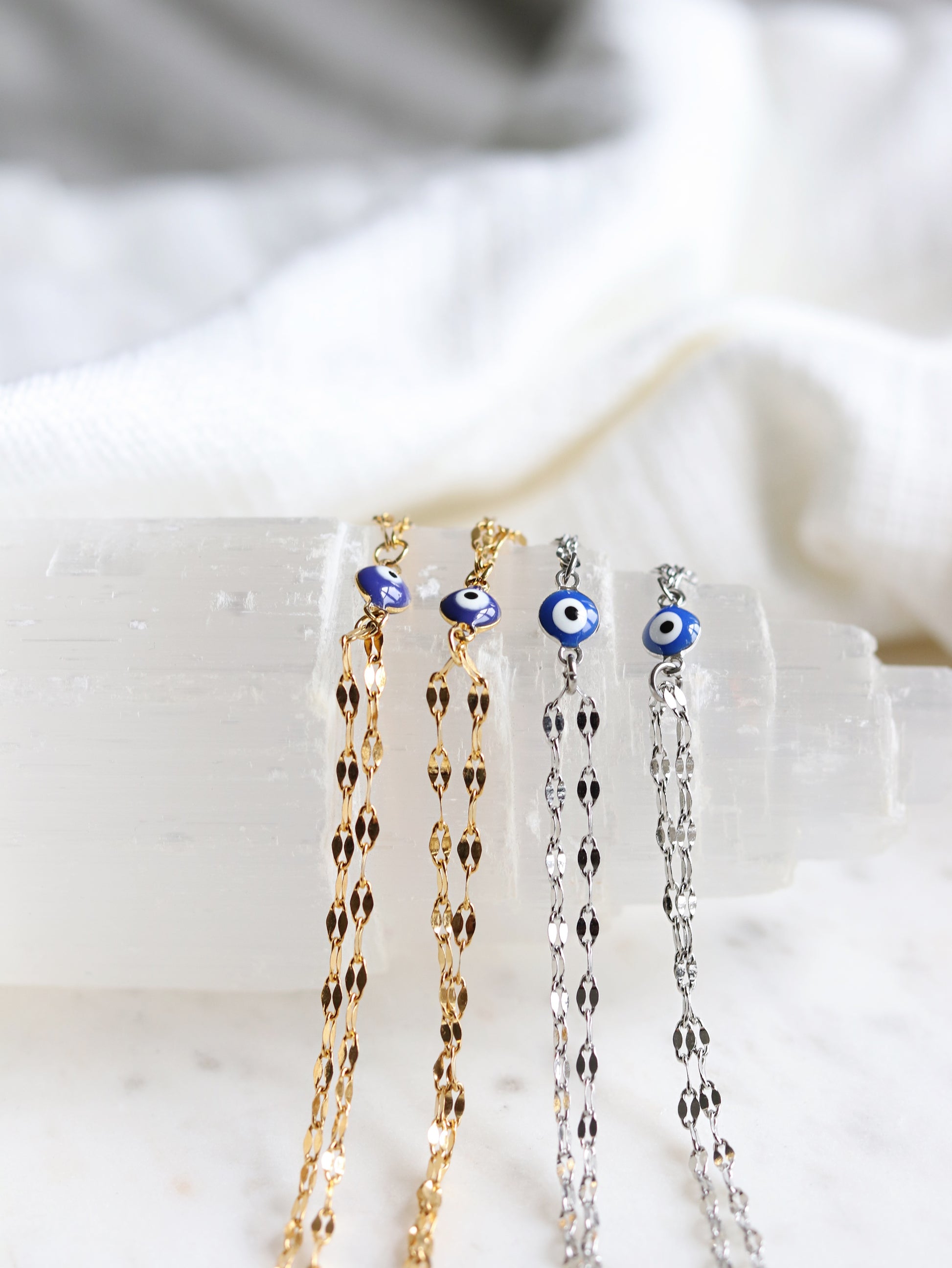 four hand chain bracelets with evil eye pendants on a white selenite slab