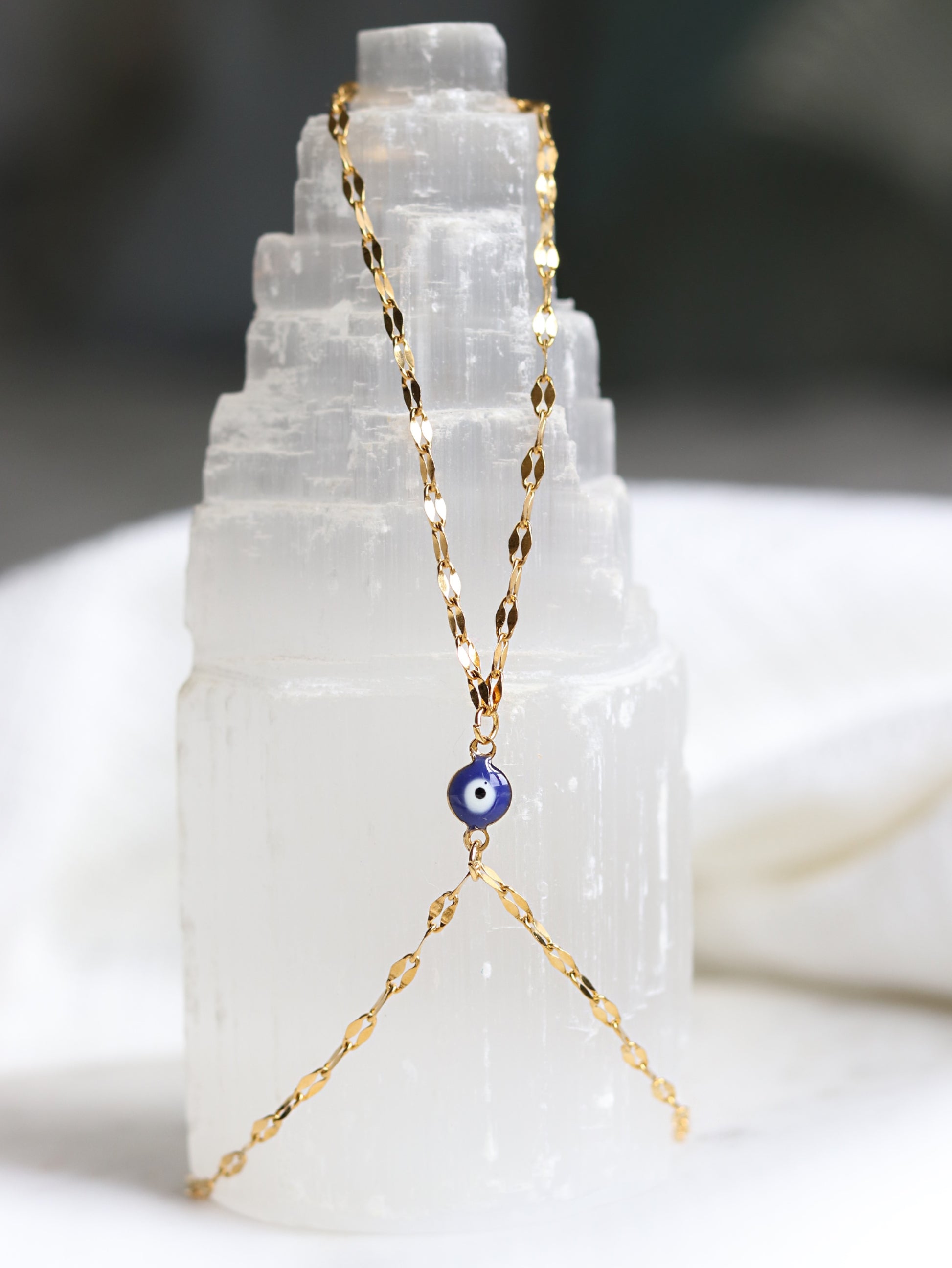 Gold hand chain bracelet with a blue evil eye pendant on a white crystal background