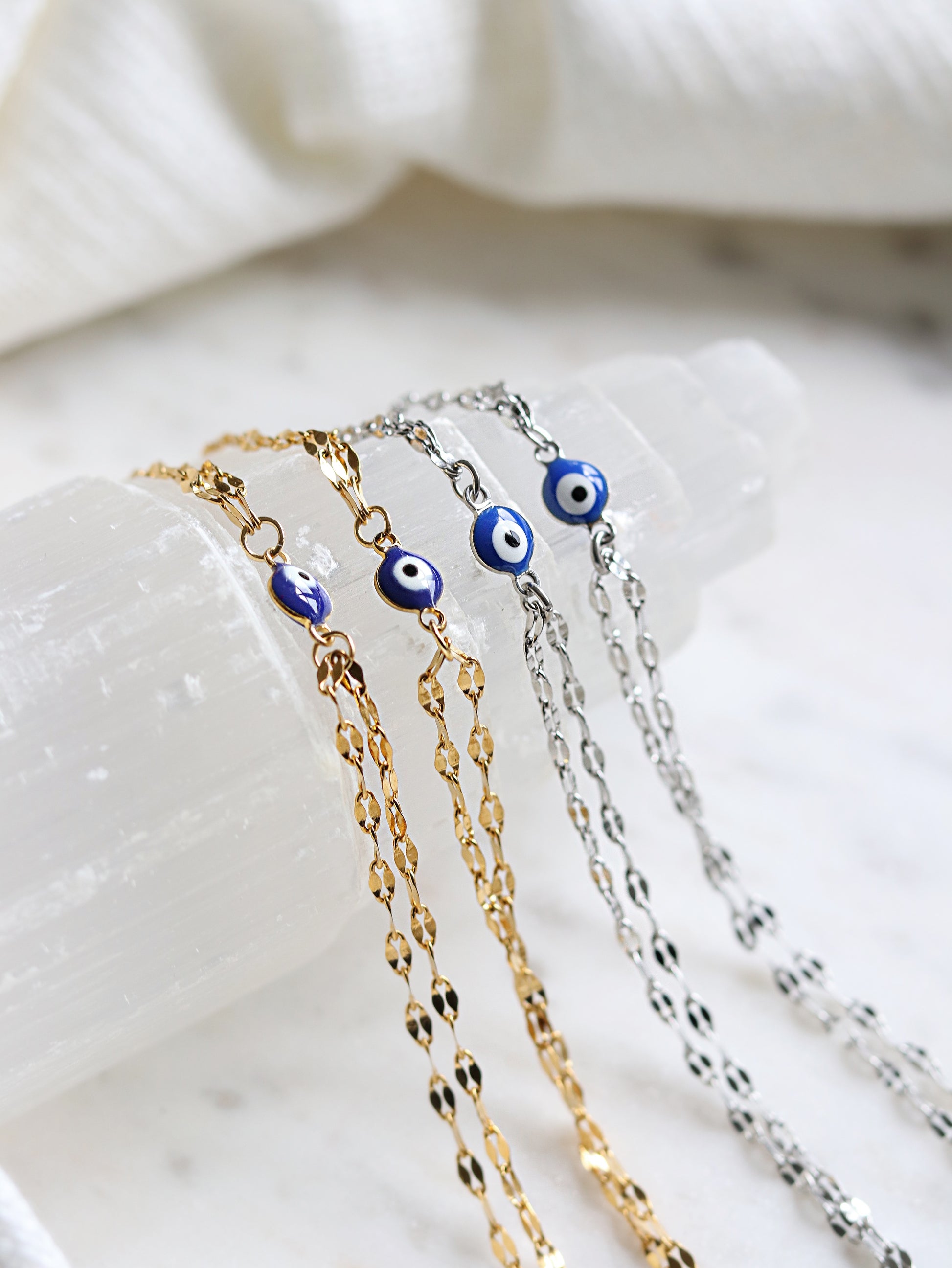 four hand chain bracelets with evil eye pendants on a white selenite slab