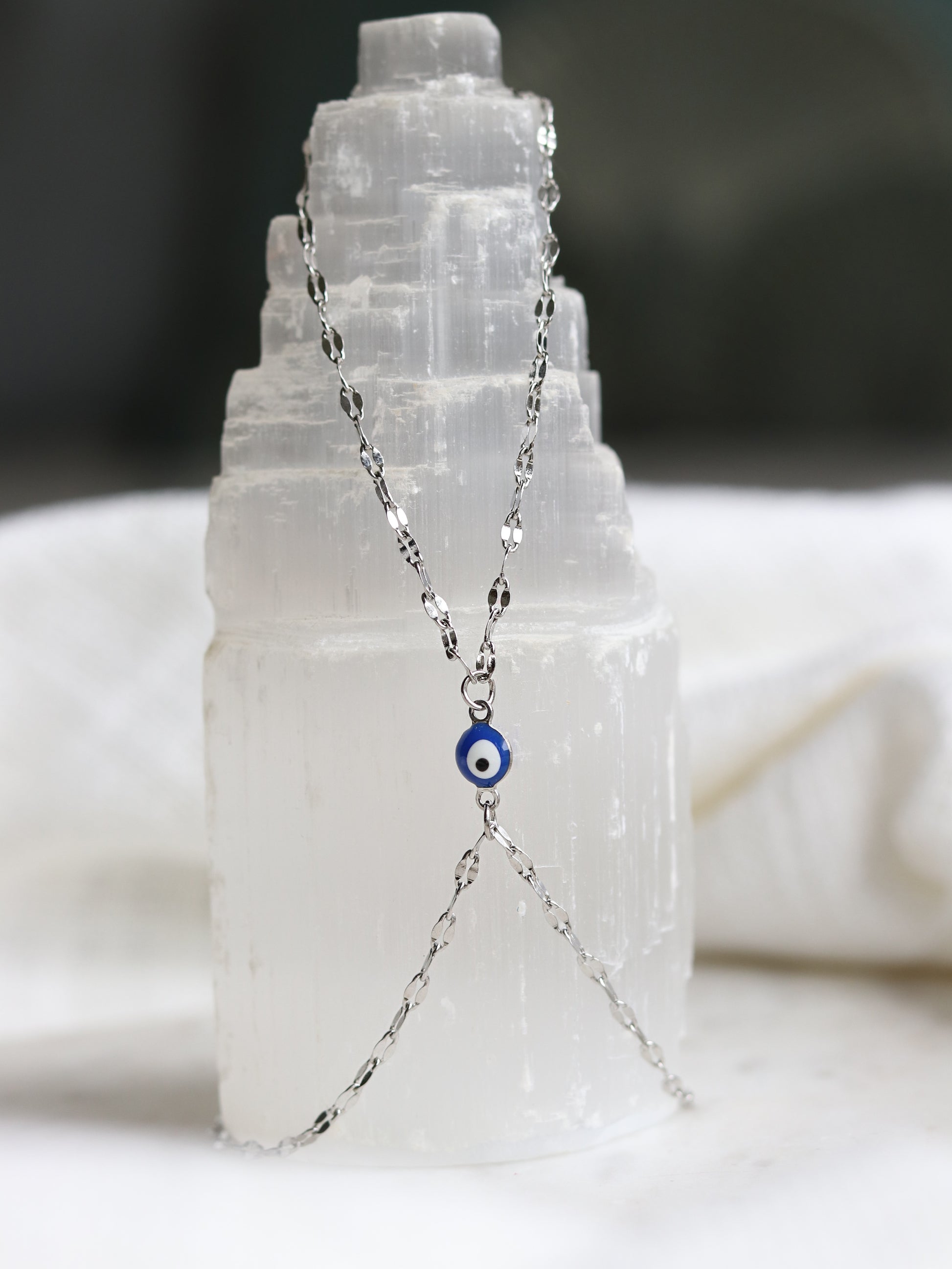 silver hand chain bracelet with a blue evil eye pendant on a selenite crystal