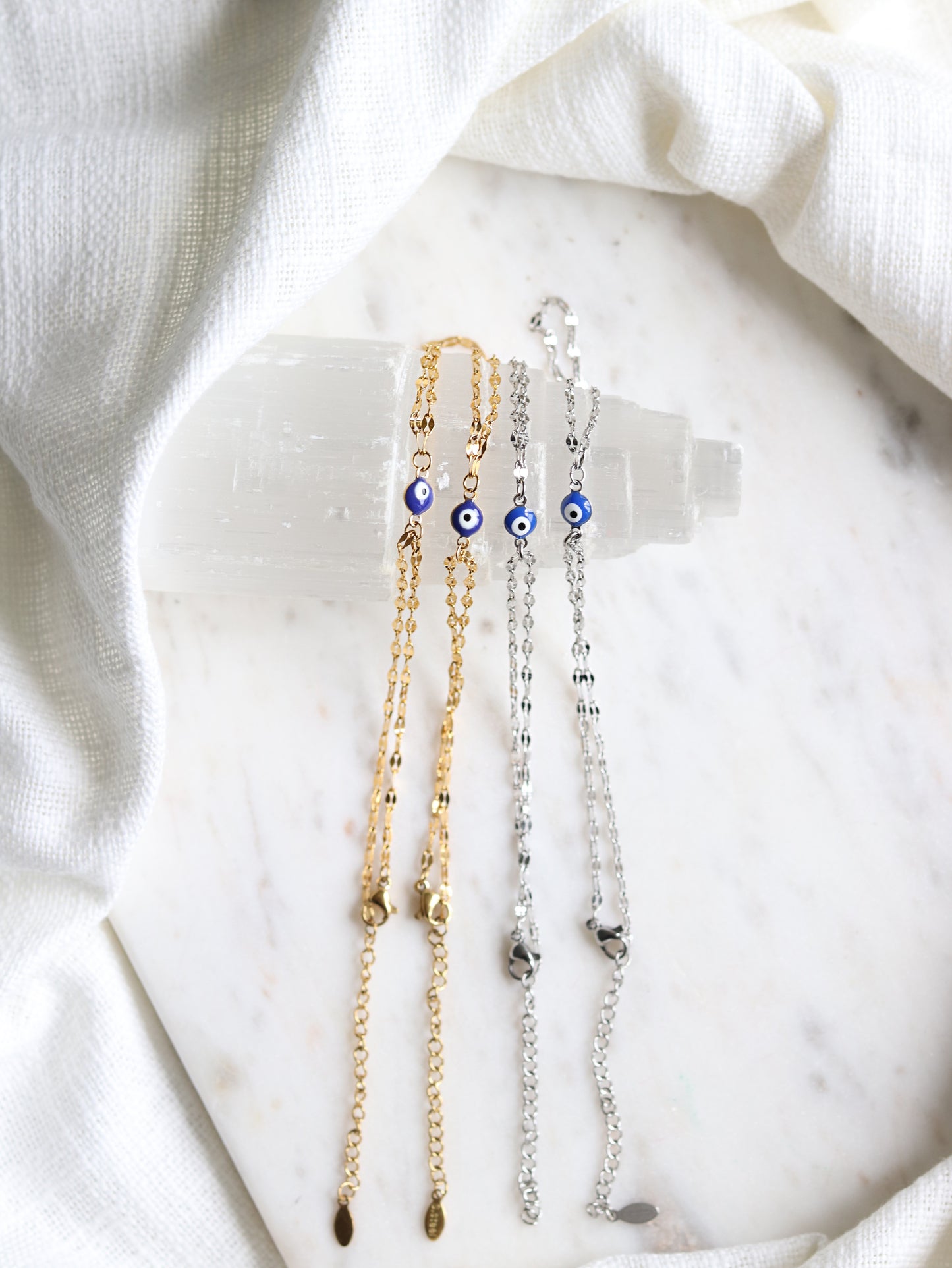 four hand chain bracelets with evil eye pendants on a white selenite slab