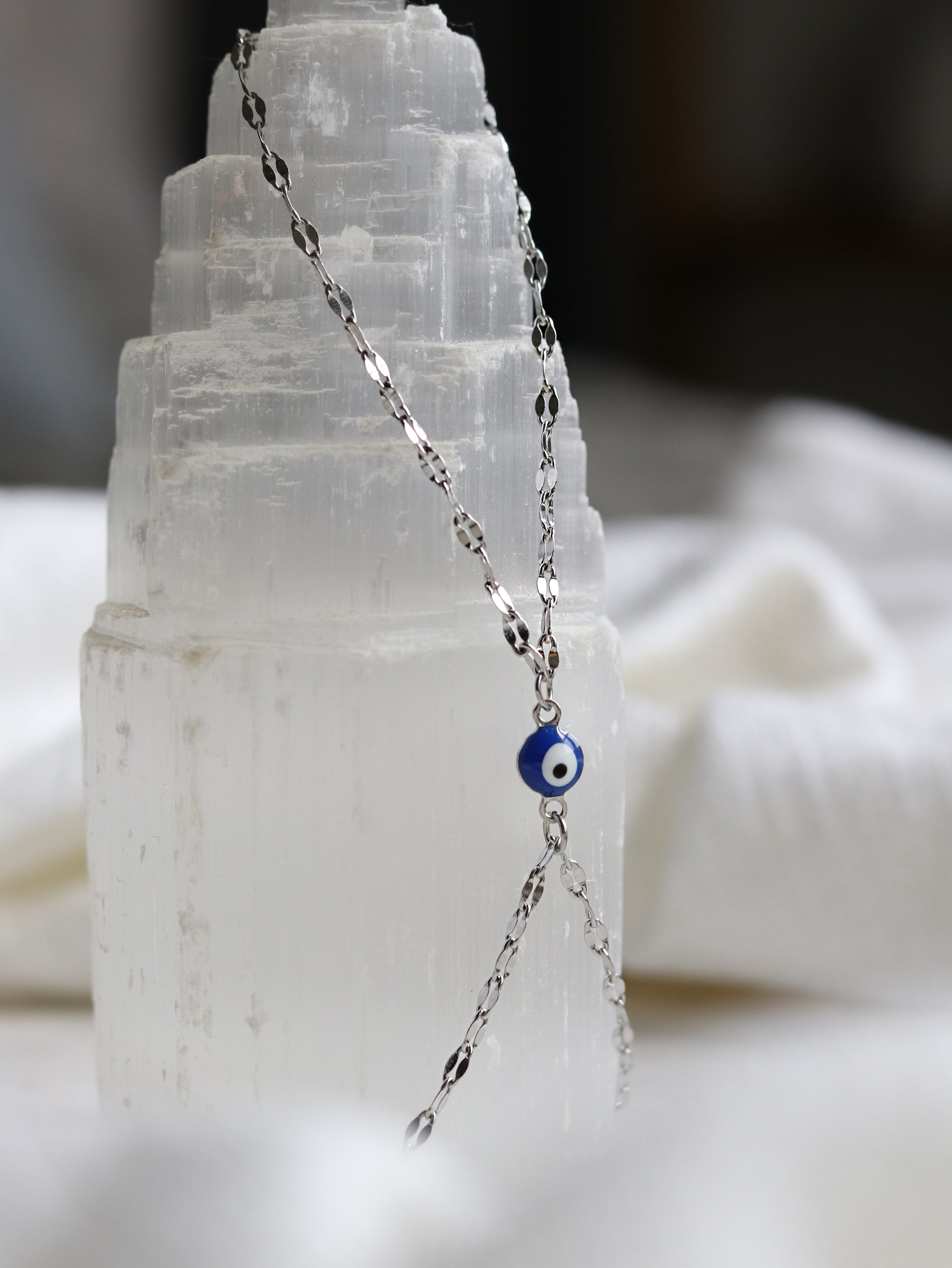 silver hand chain bracelet with a blue evil eye pendant on a selenite crystal