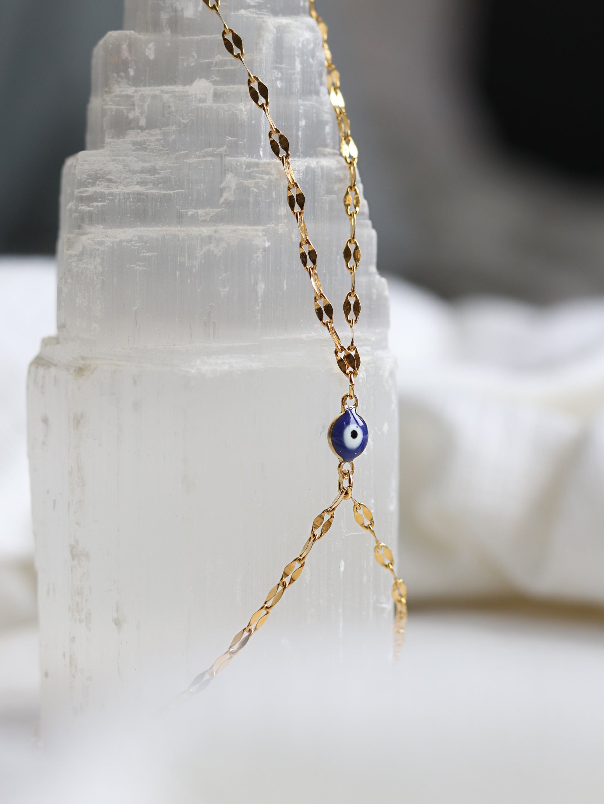Gold hand chain bracelet with a blue evil eye pendant on a white crystal background