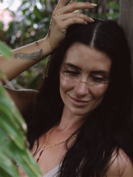 Woman with gold face and hand jewelry and tattoos in a natural setting