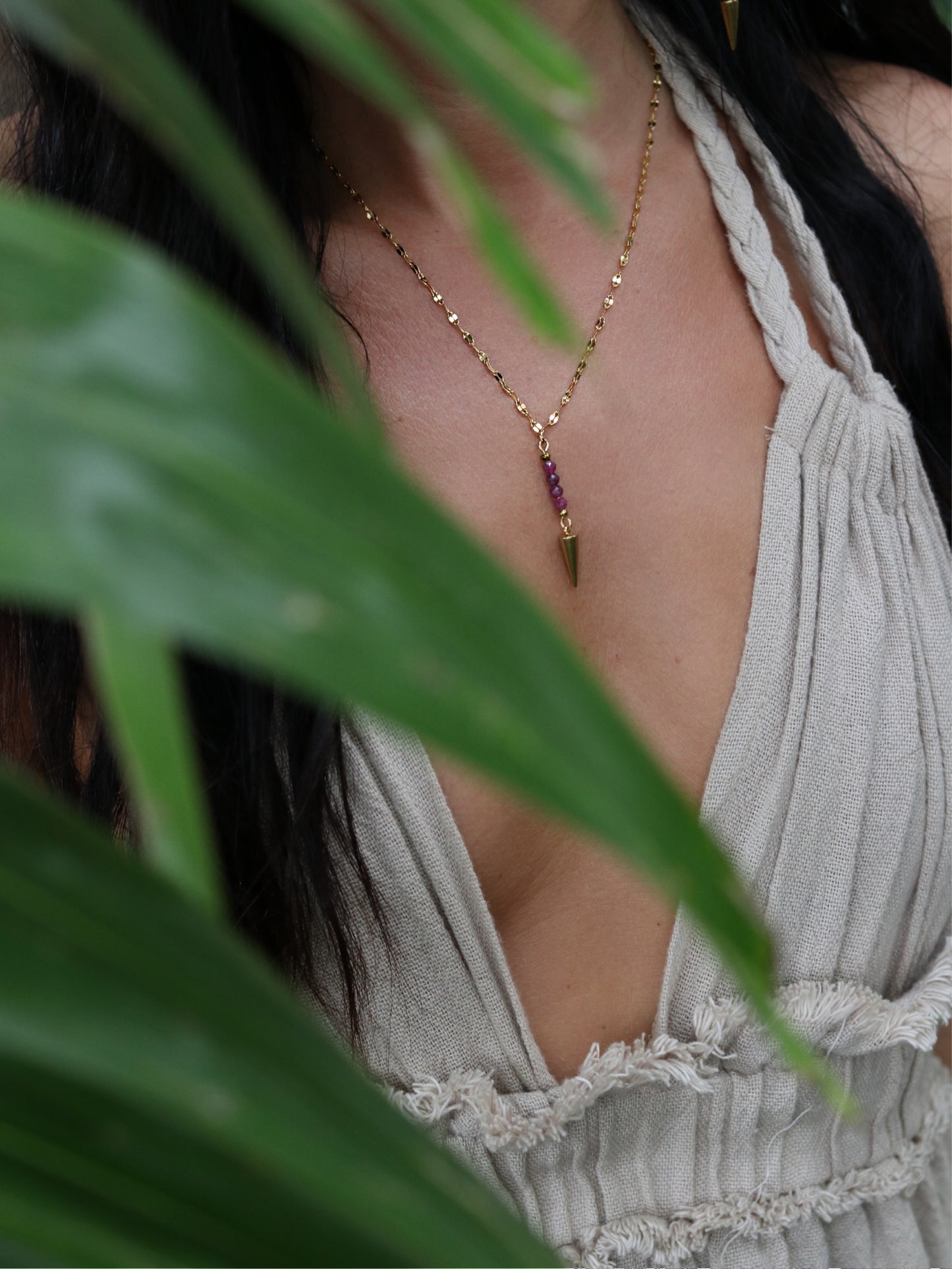 Person wearing a delicate necklace with green leaves in the foreground