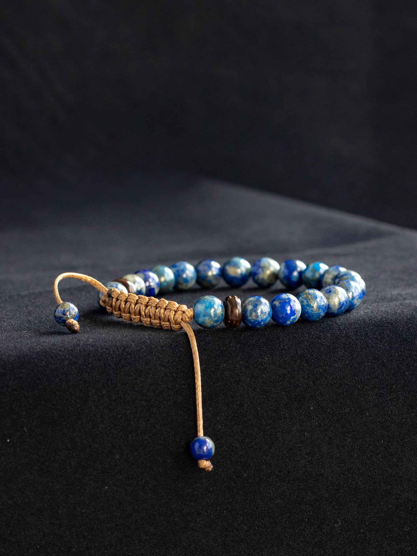 Blue beaded bracelet with a brown cord on a black background