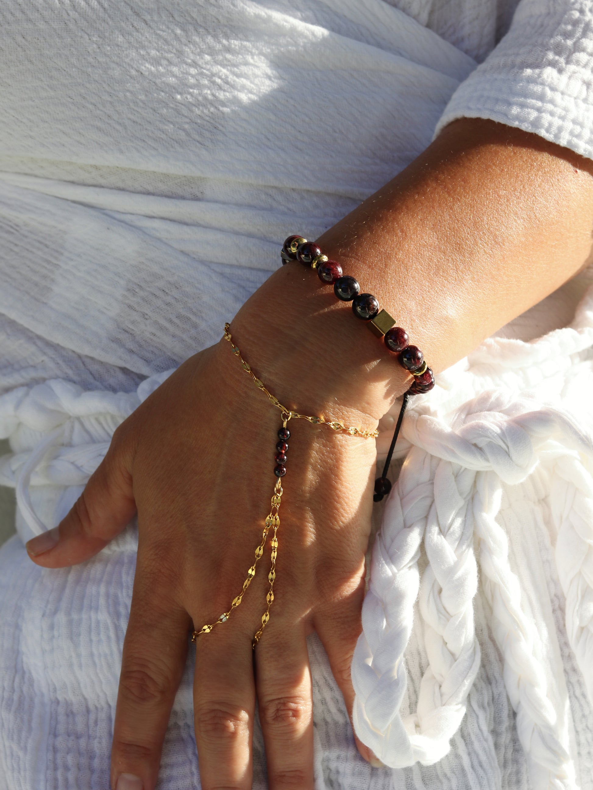 Woman wearing red garnet hand chain bracelet showing passionate gemstone beads and gold connecting chain