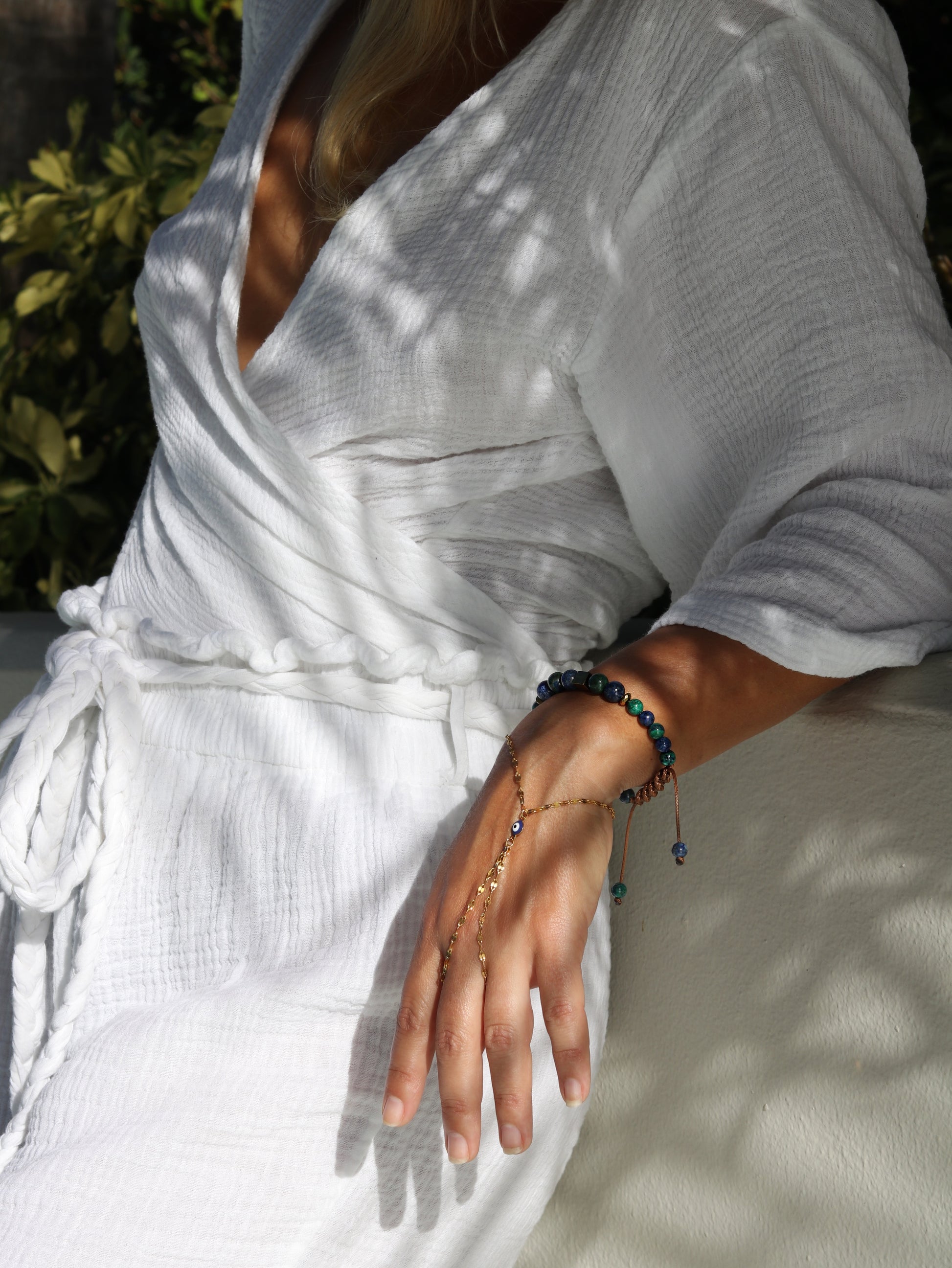 Person wearing a white organic clothes with a close-up of their hand adorned with evil eye charm hand chain bracelet