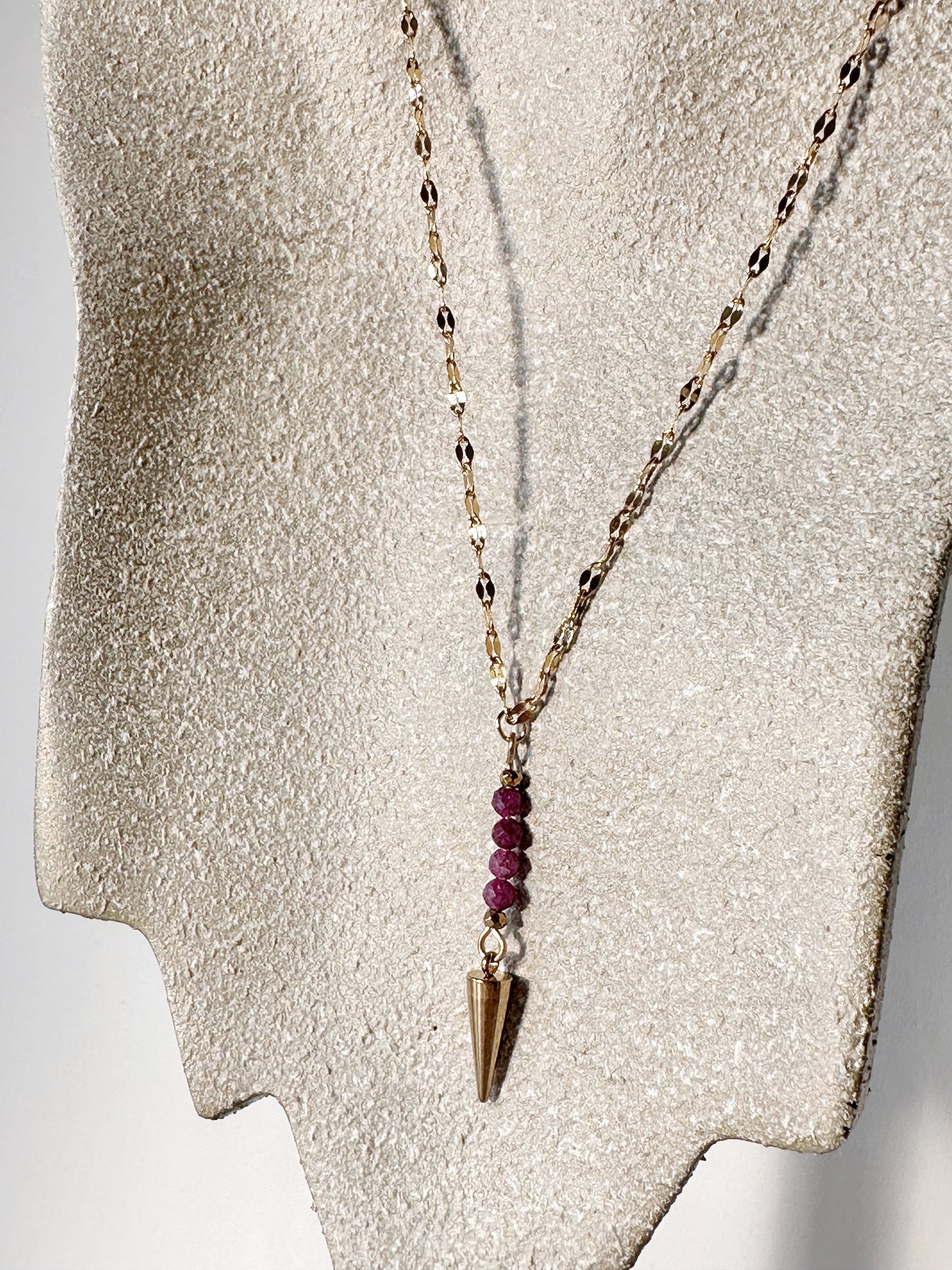 Necklace with red ruby beads and a gold pendant on a textured gray surface