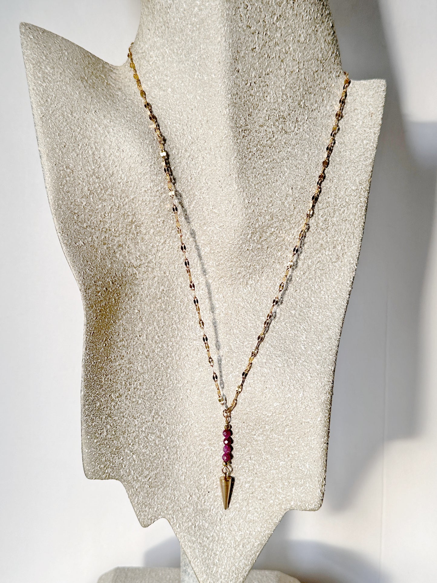 Necklace with a gold chain and red ruby beads on a gray stand