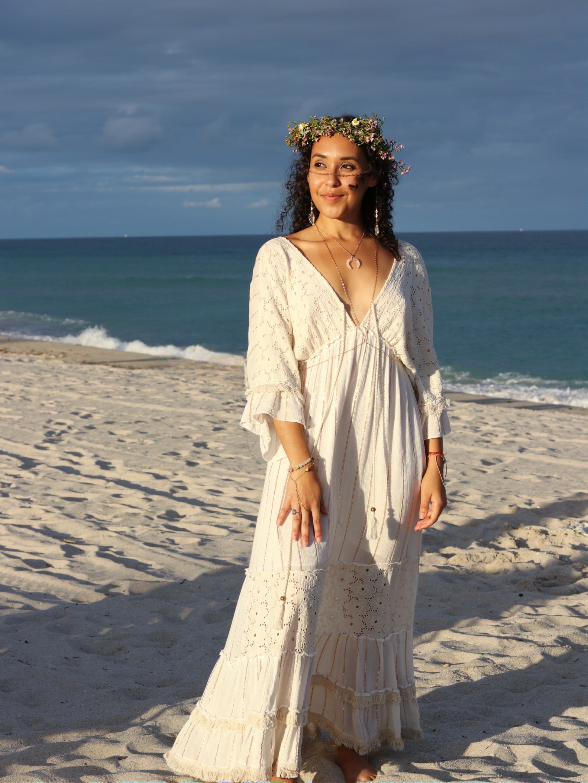 Woman in a white dress standing on a beach with ocean waves in the background