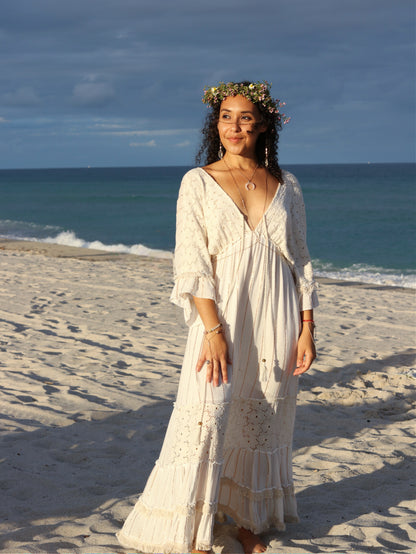 Woman in a white dress standing on a beach with ocean waves in the background
