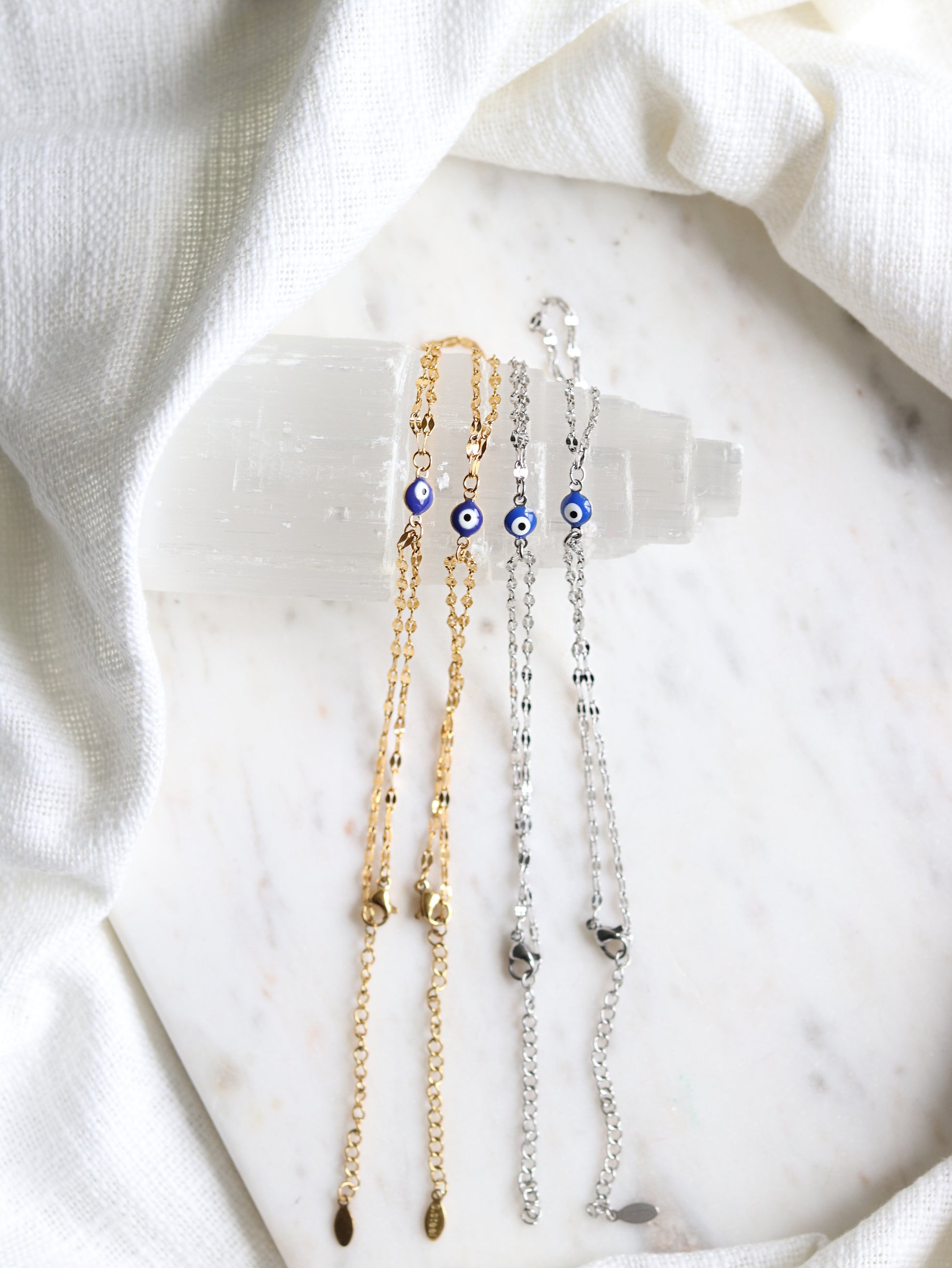 four hand chain bracelets with evil eye pendants on a white selenite slab