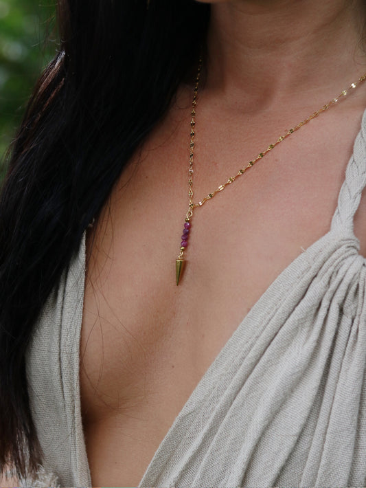 Necklace with a gold pendant and natural ruby beads worn by a person in a light-colored top.