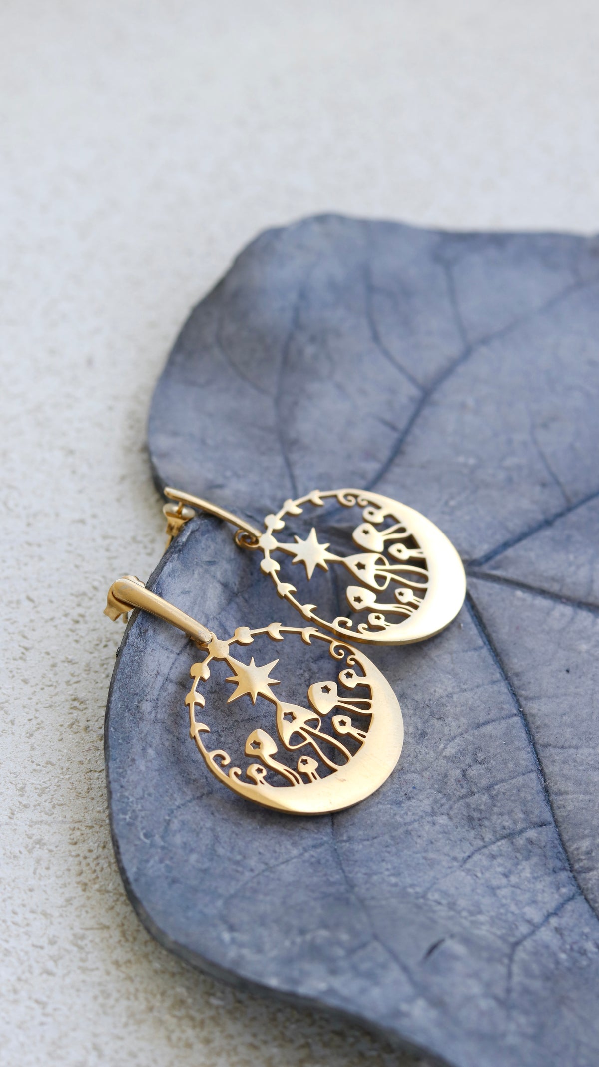 Woman at beach wearing gold mushroom dangle earrings styled with layered gold necklace — nature-inspired 18k gold plated earrings by BURZAN Design
