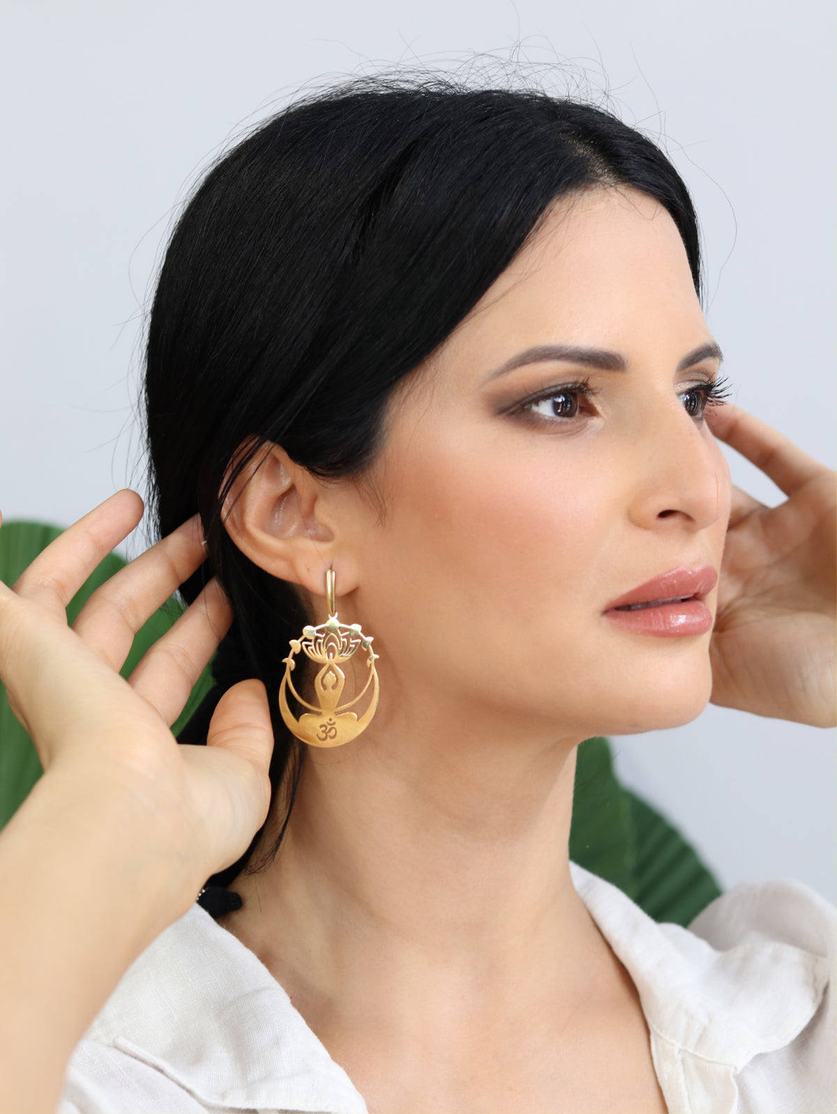 Woman wearing gold lotus drop earrings with Om symbol — spiritual statement jewelry by BURZAN Design, Miami