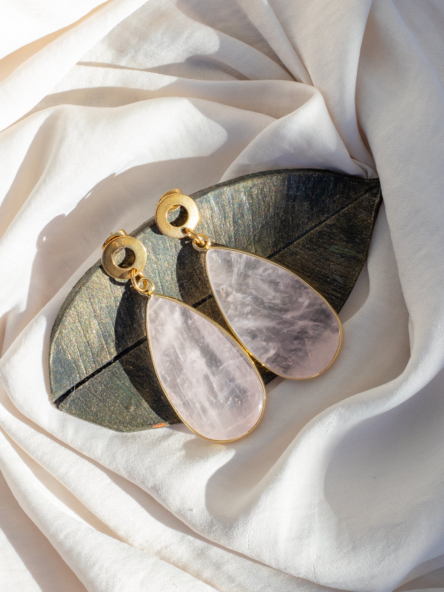 Pair of Rose Quartz earrings with gold accents on a white fabric background