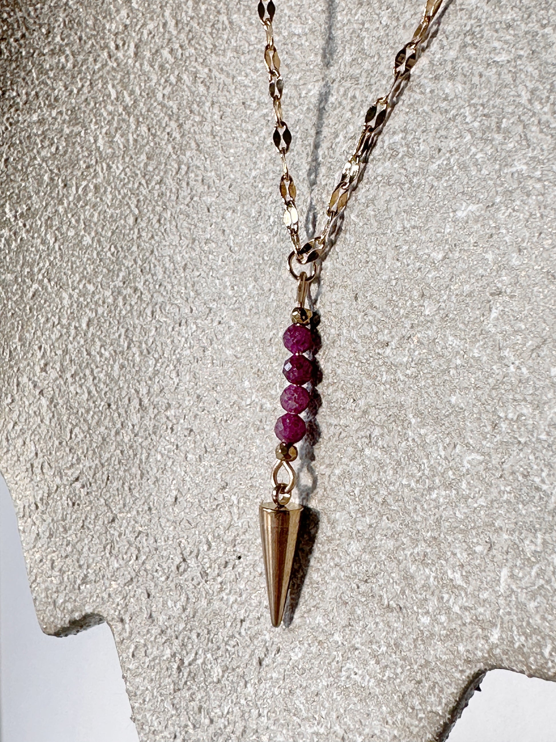 Necklace with red beads and a gold pendant on a textured gray background